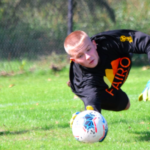 GOALKEEPER is diving for the ball with a fairo Shirt on